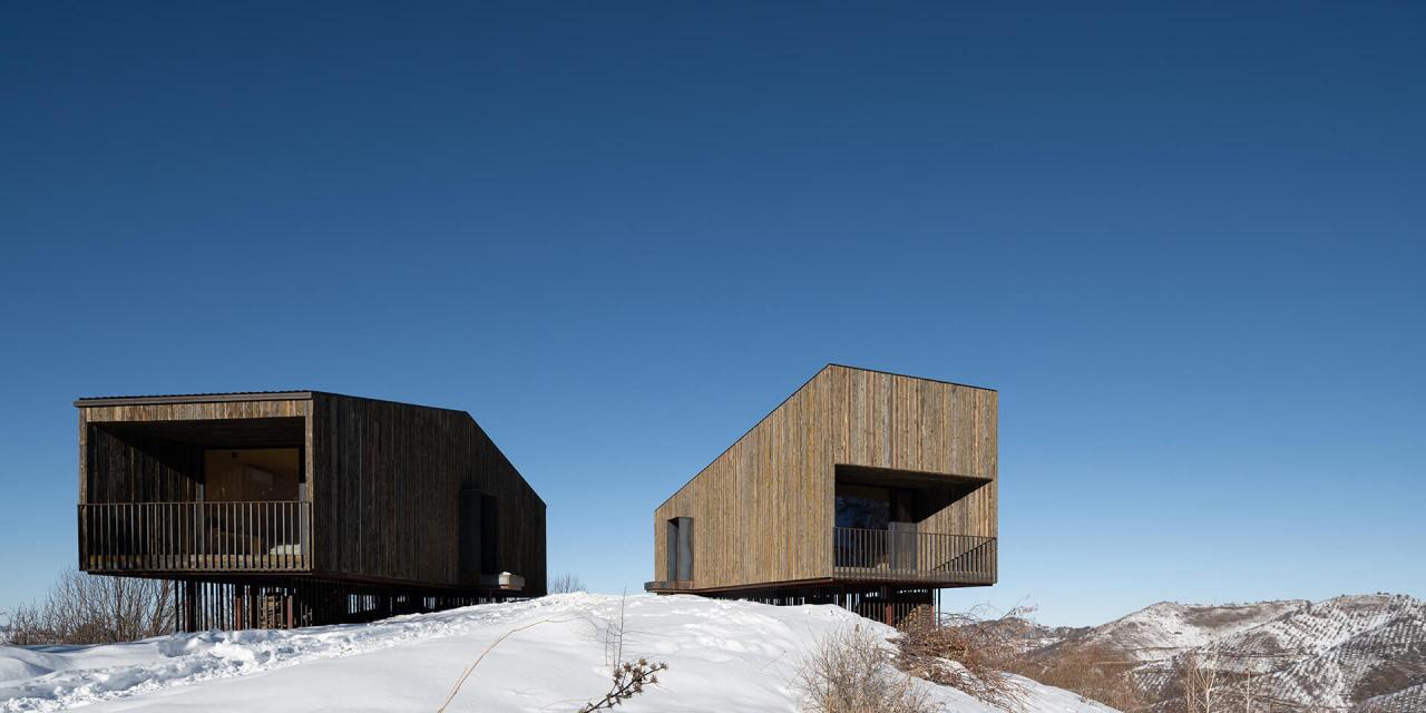Cele doua cabane AUM pe dealul inzapezit din muntii Almaty, Kazahstan, cu fatade din lemn de larice negrit