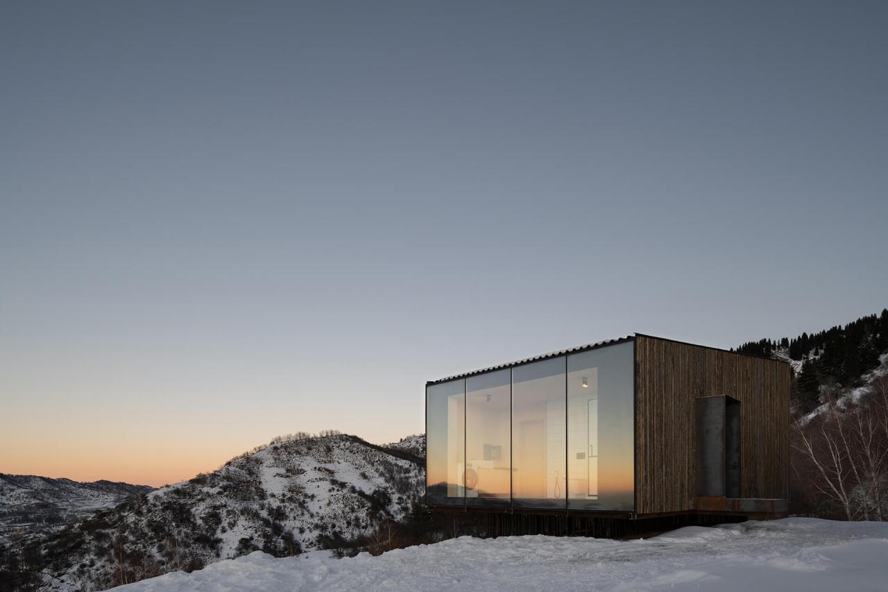 Cabana AUM la apus de soare cu fereastra panoramica care reflecta cerul portocaliu si muntii