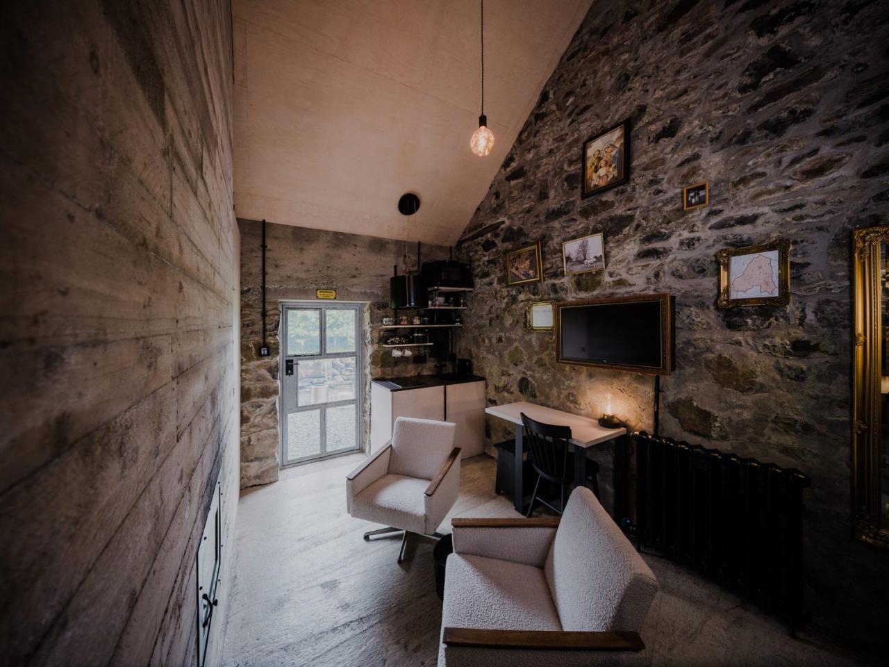 Interior casa veche din piatra cu fotolii albe, perete de piatra, tablouri si becuri suspendate