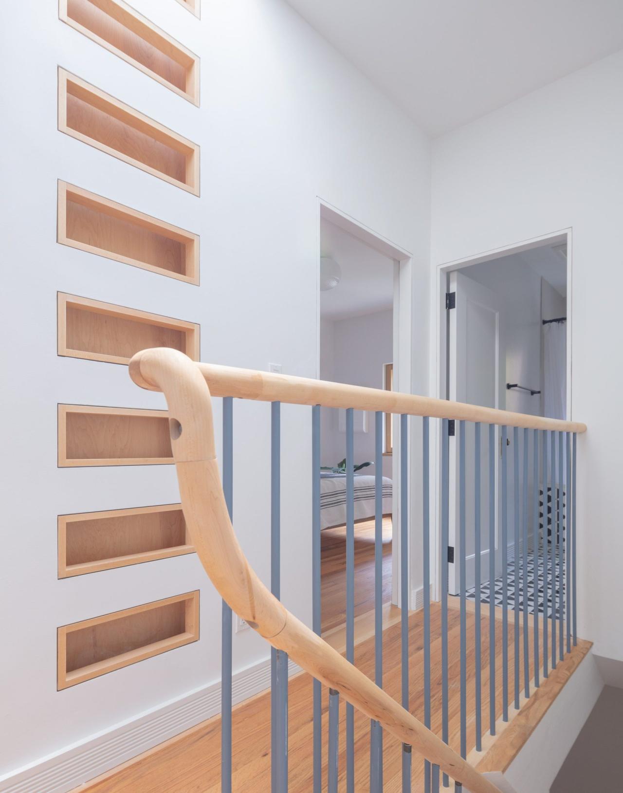 Hol etaj cu balustrada din lemn deschis si bare metalice gri, rafturi rectangulare din lemn integrate in perete