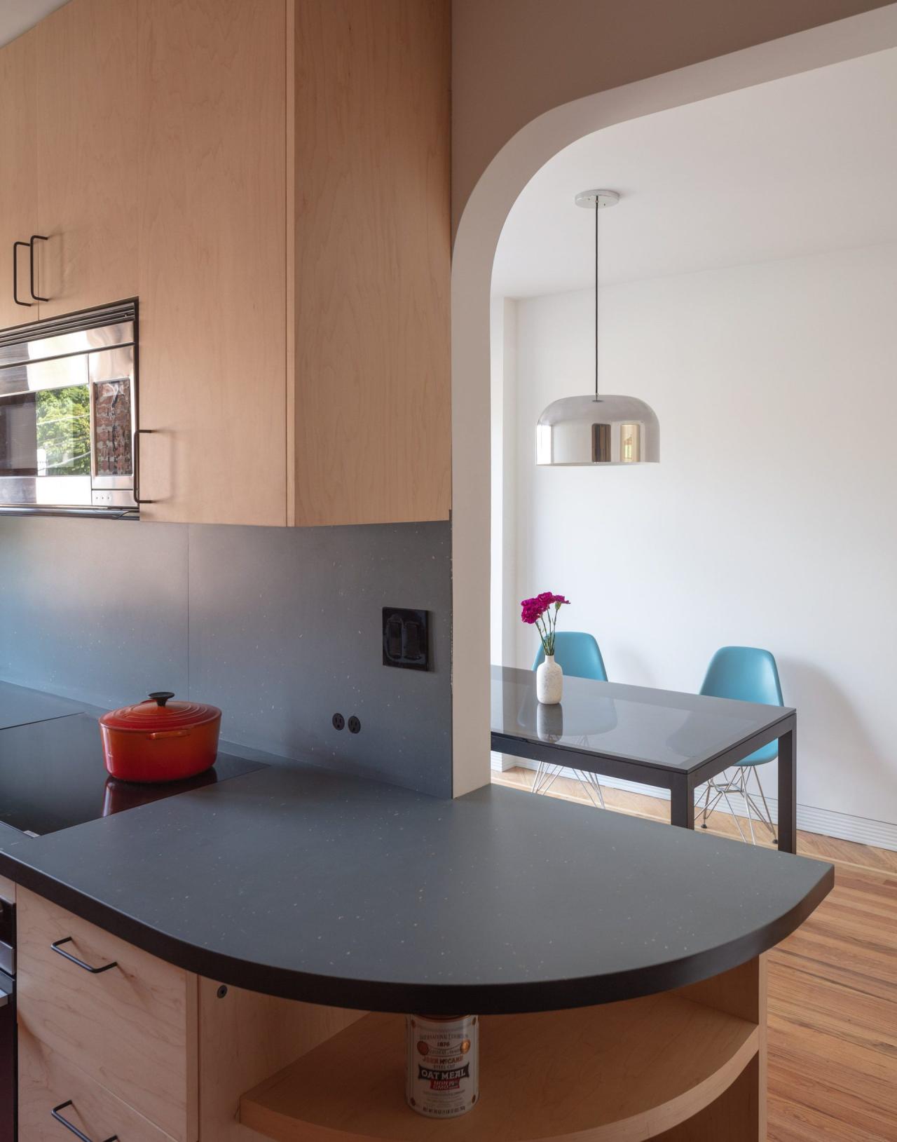 Vedere din bucatarie spre zona de dining prin arc rotunjit - masa neagra cu scaune albastre Eames, lampa suspendata cromata