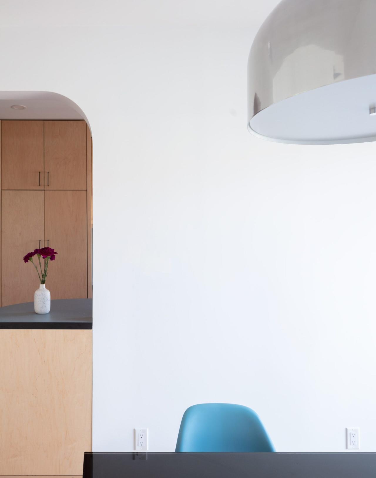Detaliu zona de dining cu scaun albastru Eames, lampa suspendata cromata si vedere spre bucatarie prin arc