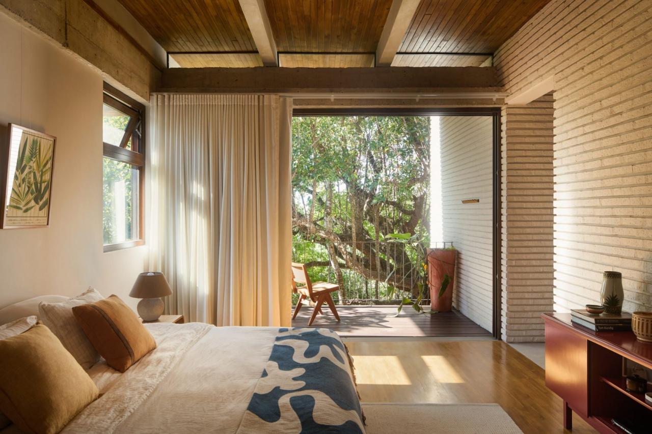 Dormitor master cu pat dublu, cuvertura albastra cu model, tavan din lemn si deschidere larga spre terasa cu copaci pochote – foto Thibault Cartier / Dezeen