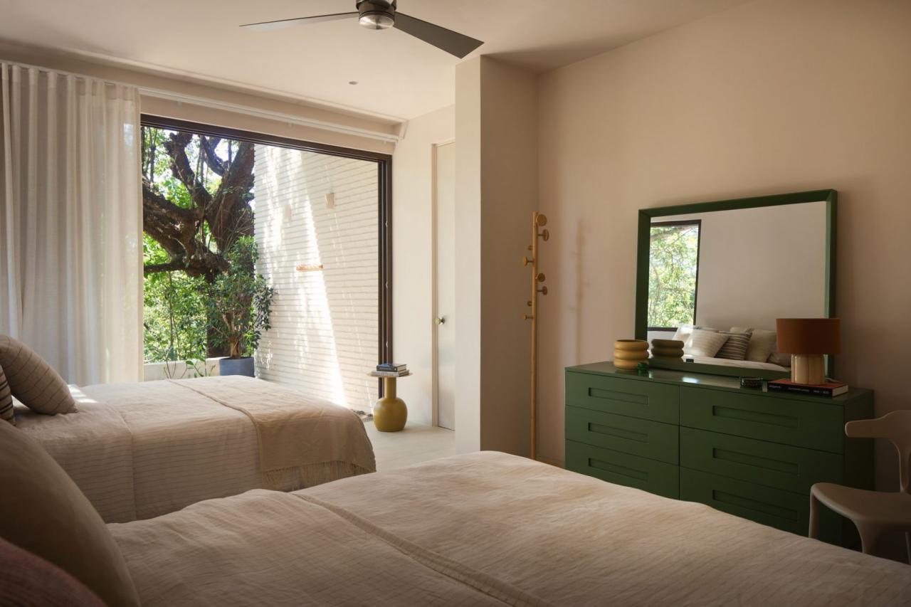 Dormitor cu doua paturi simple, comoda verde inchis cu oglinda si usa glisanta spre terasa cu copaci – foto Thibault Cartier / Dezeen