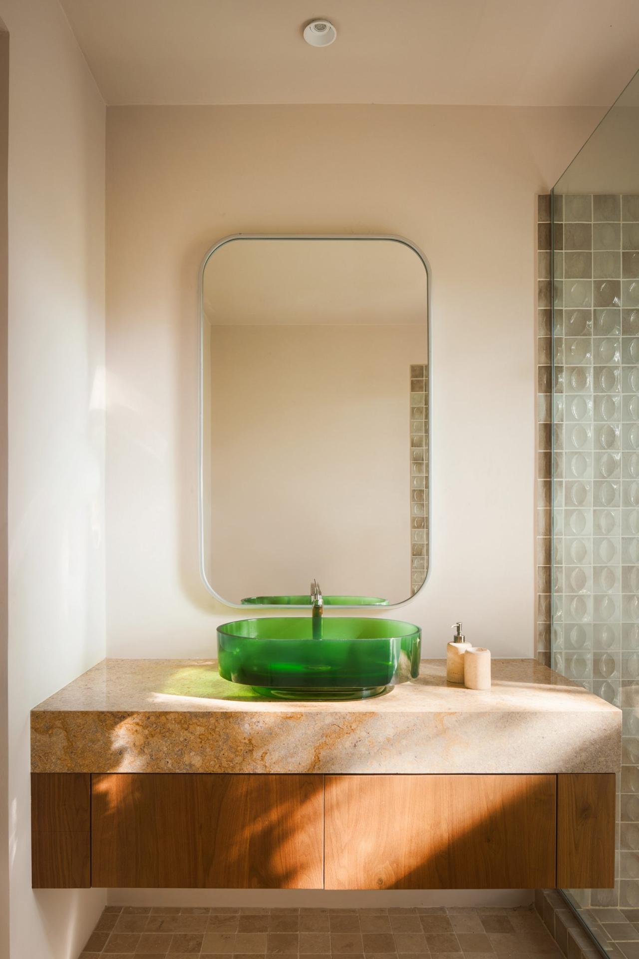 Baie cu chiuveta din sticla verde pe blat de travertin, oglinda rotunjita si perete cu faianta texturata – foto Thibault Cartier / Dezeen