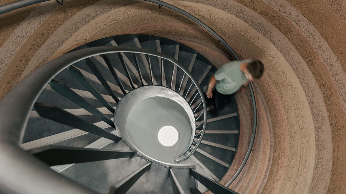 Vedere de sus a scarii spirale din interiorul turnului de pamant compactat, cu pereti stratificati in nuante de ocru – foto Chris Wharton / M Moser Associates