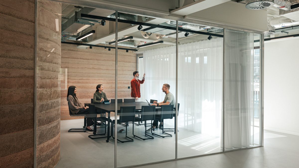 Sala de conferinte cu pereti de sticla, masa neagra si perete din pamant compactat, echipa in sedinta – foto Chris Wharton / M Moser Associates