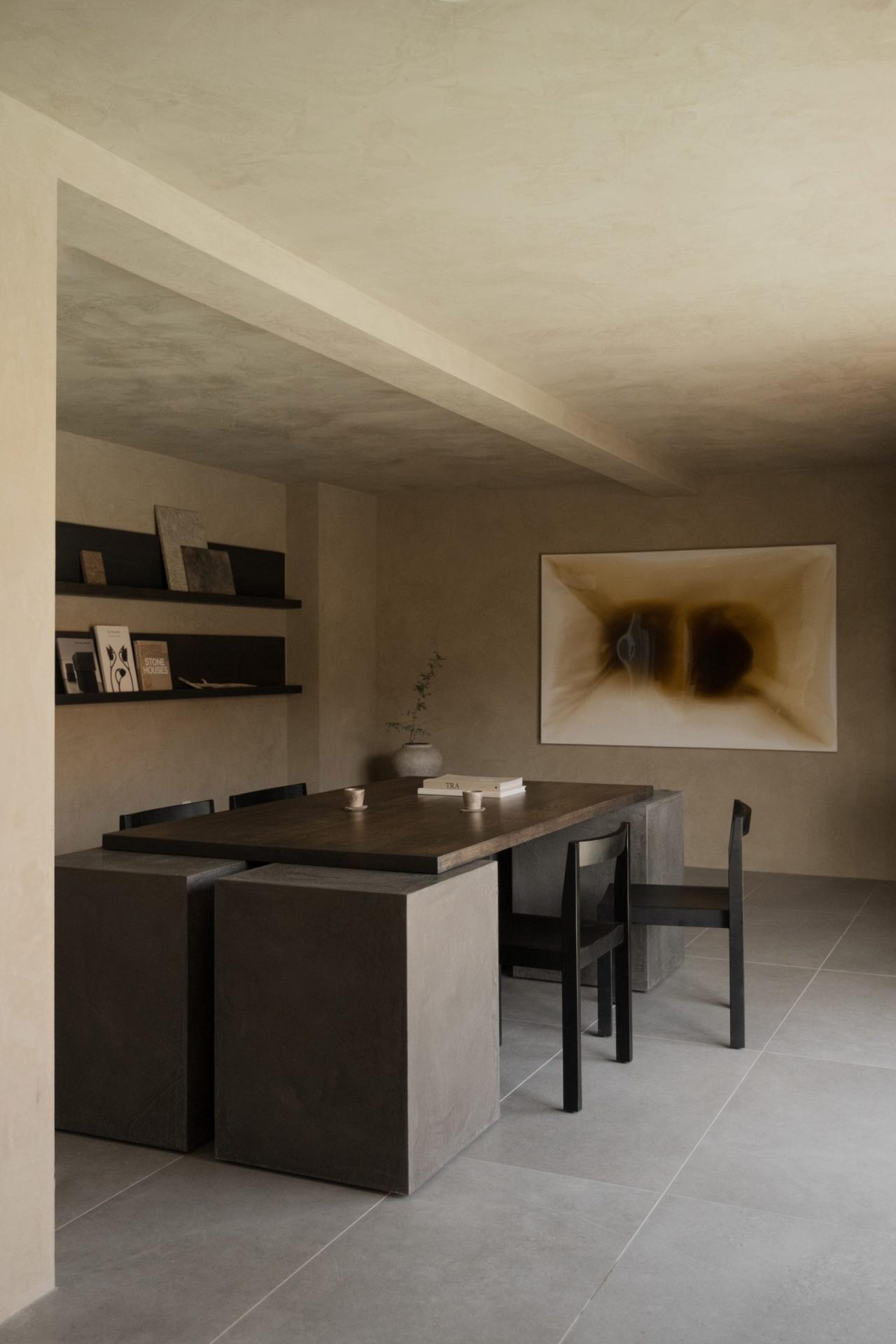 Zona de dining cu masa intunecata, rafturi si tablou abstract in zona comuna a hotelului