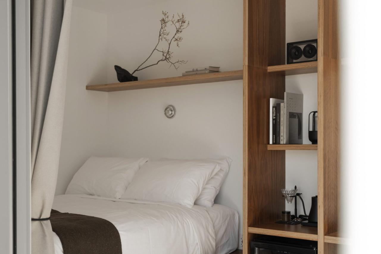 Camera de hotel cu pat alb, raft din lemn si biblioteca cu carti si echipamente audio