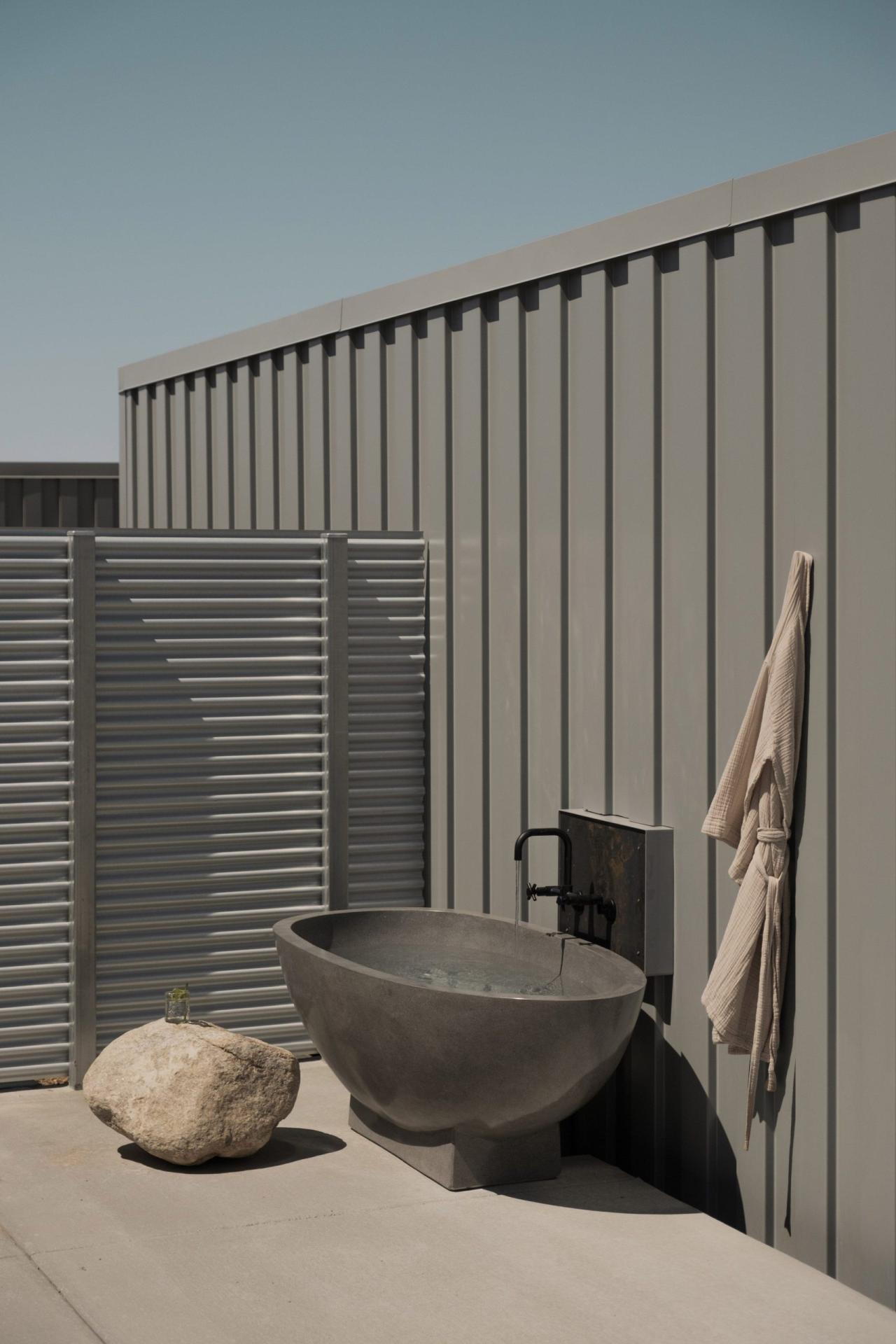 Baie exterioara cu cada din beton si perete de container gri - spatiu wellness privat