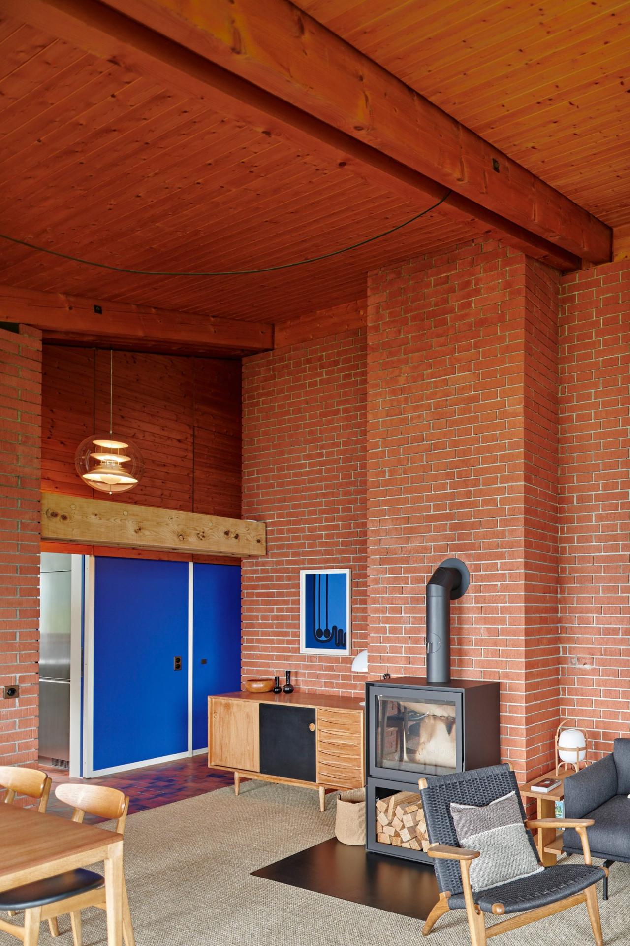 Zona de living a casei din Vernate cu soba din fonta, fotolii din lemn si usa albastra Le Corbusier