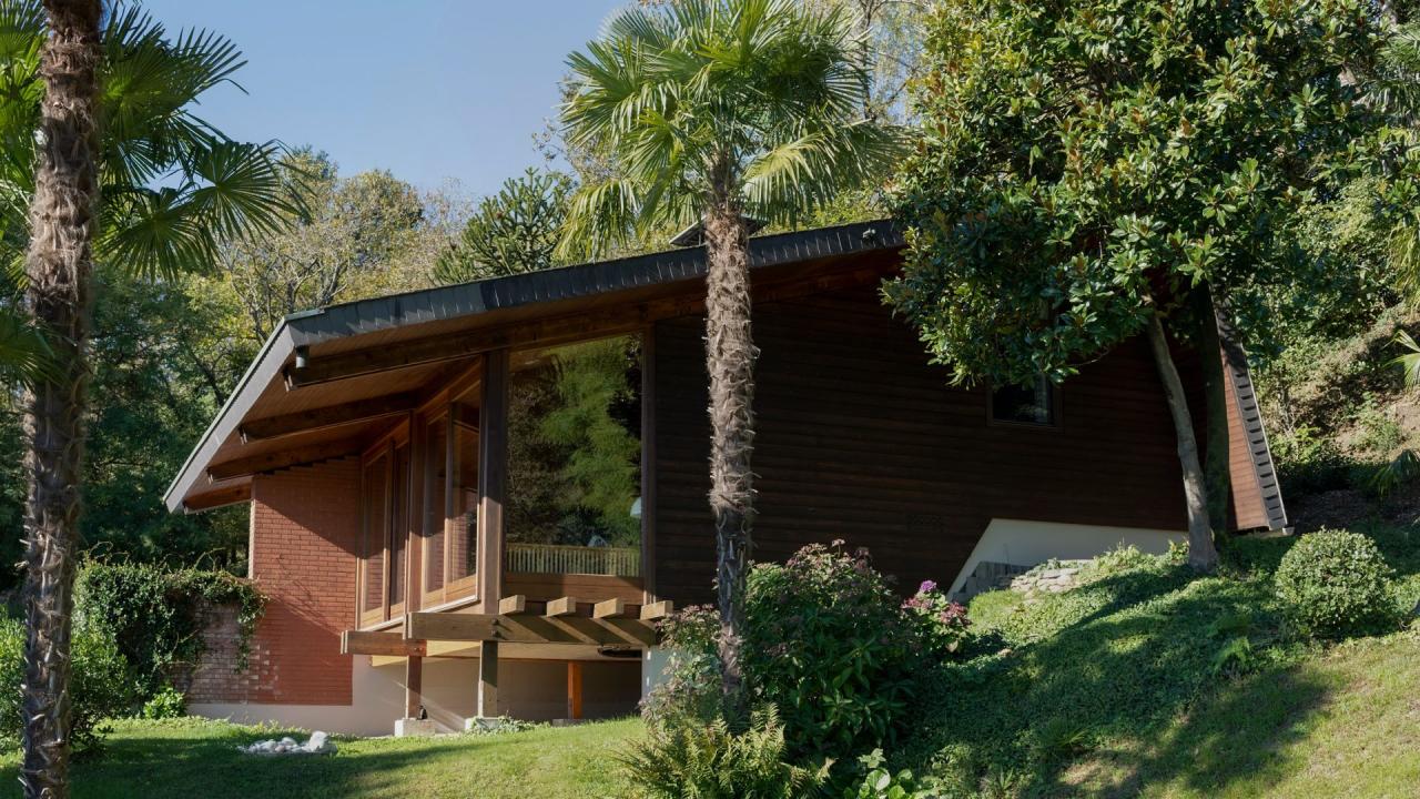 Vedere exterioara a casei din Vernate cu piscina, fatada din caramida si gradina cu palmieri