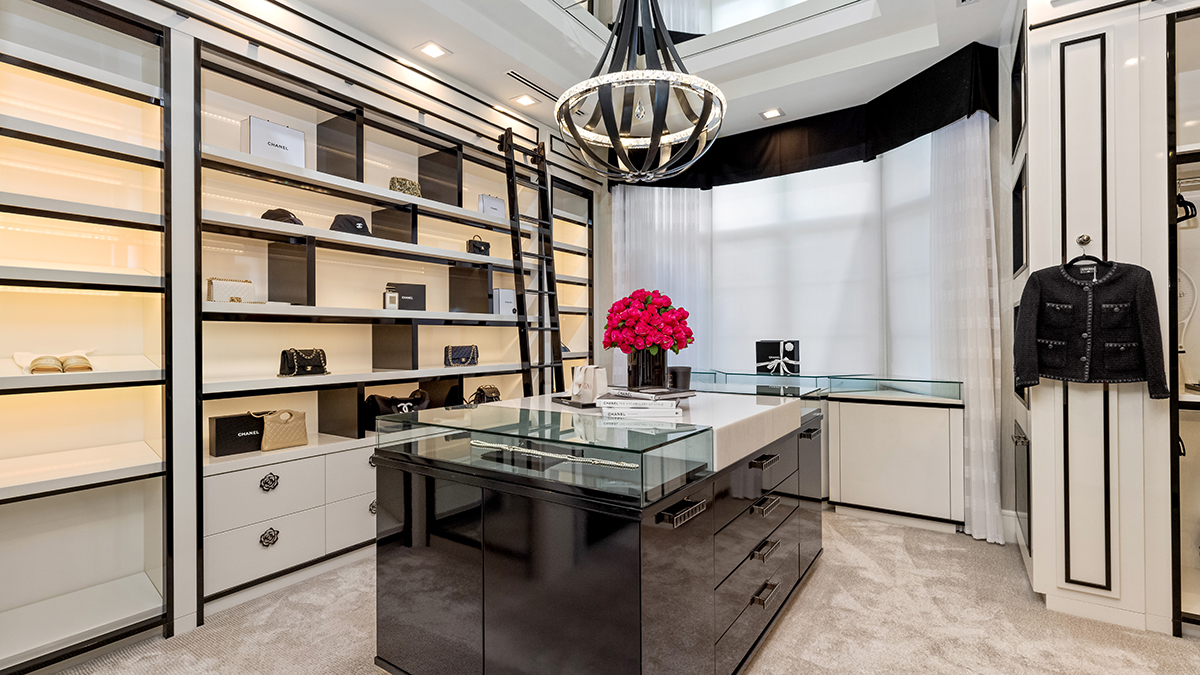 Walk-in closet de lux cu rafturi iluminate cu genti Chanel si insula centrala cu vitrina